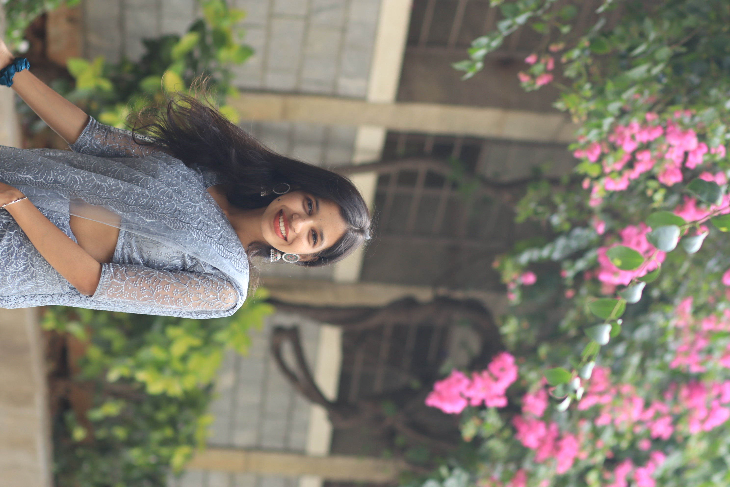 A smiling woman in a grey sari beneath bougainvillea